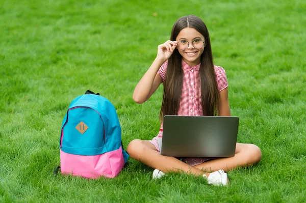 Teen girl utilizzare il computer su erba verde nel parco. bambino con zaino e taccuino. nuove tecnologie nella vita moderna. studio. bambino felice in occhiali che lavora su computer portatile. educazione online. torna a scuola — Foto Stock