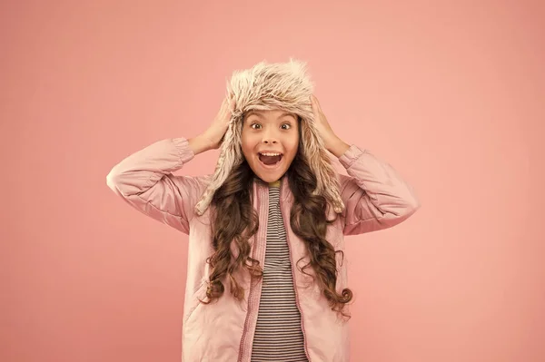 Niña juguetona usar sombrero de piel con orejeras fondo rosa. Accesorio peludo suave. Niño pelo largo sombrero de piel suave disfrutar de la suavidad. Concepto de moda de invierno. Sombrero cálido para clima frío. Tendencia de piel sintética — Foto de Stock