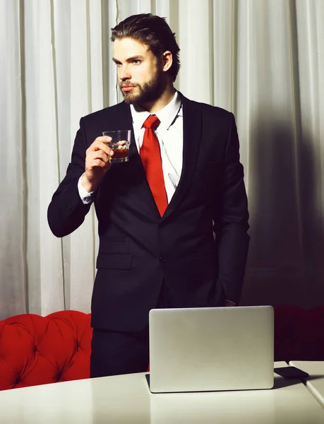 Barbudo, hombre de negocios con vaso de whisky, teléfono celular, portátil — Foto de Stock
