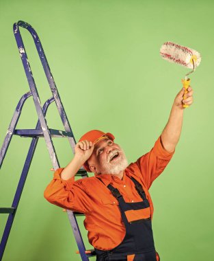 Kıdemli boyacı merdivende paten kullanır. Duvarı yeşile boyamak. İş kıyafetleri içinde profesyonel bir ressam. Odada duvar boyama işçisi. Tekerlekli erkek dekoratör