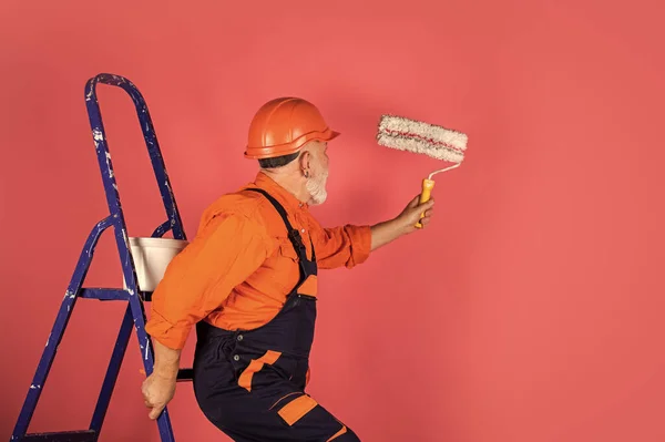 Bouwvakker schilderen gevel. thermische isolatiewerkzaamheden. Schildertrap. Om reparaties uit te voeren. Een man in werkkleding die muur schildert in een lege kamer. schilder in het algemeen en kap met verfemmer — Stockfoto