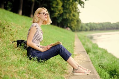 Kız nehir kenarındaki yeşil çimlerde oturuyor. Tatil sezonu. Yaz tatili. Kız iş gününden sonra nehir kenarında dinleniyor. Tatil hayali kuran kadın. Dinlen ve hobi olarak dinlen. Kendine zaman ayır.