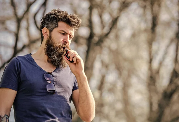 Man long beard relaxed with smoking habit. Man with beard and mustache breathe out smoke. Stress relief concept. Bearded man smoking vape. White clouds of flavored smoke. Smoking electronic cigarette