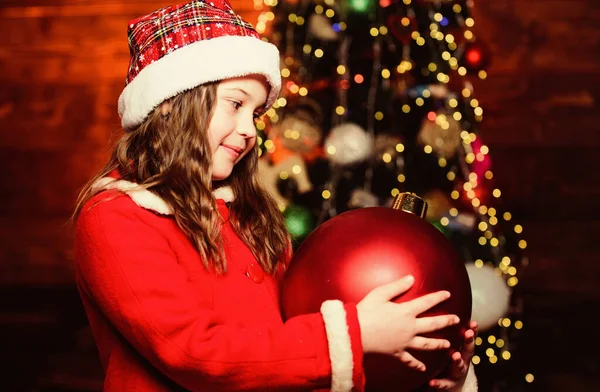 Festive atmosphere christmas day. Girl santa claus costume hold big ball christmas tree ornaments. Christmas decorations. Love to decorate everything around. Merry christmas. Sparkling big toy