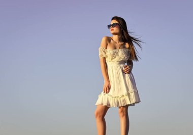 Harika bir tarzı var. Mavi gökyüzünde poz veren mutlu genç kadın. Güneş gözlüklü güzel bir kadın. Yazlık kıyafet. Güzel kızın portresi. Plaj tarzı. Yazın açık hava yaşam tarzı