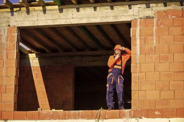 Tamirci olay yerinde kask takıyor. Yorgun müteahhit. Sigara içen inşaat işçisi. Bina yapım aşamasında. Üniformalı ve kasklı sakallı adam. Sıradan çalışma günü