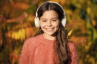 Çocuklar için eğitici ve indirilebilir sesli kitaplar. Küçük kız kulaklıklarla sonbahar ağacının yanında dinleniyor. Sonbahar havası için müzik. Dinleme şarkısı. Sonbahar gününün tadını çıkar. Güzel şarkılarla sonbahar yürüyüşleri