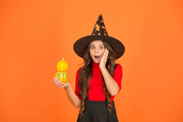Surprised kid wear witch hat. child with small pumpkin. teen girl has long curly hair and wear dress for party celebration. autumn season holiday. childhood leisure. jack o lantern. happy halloween — Stock Photo, Image