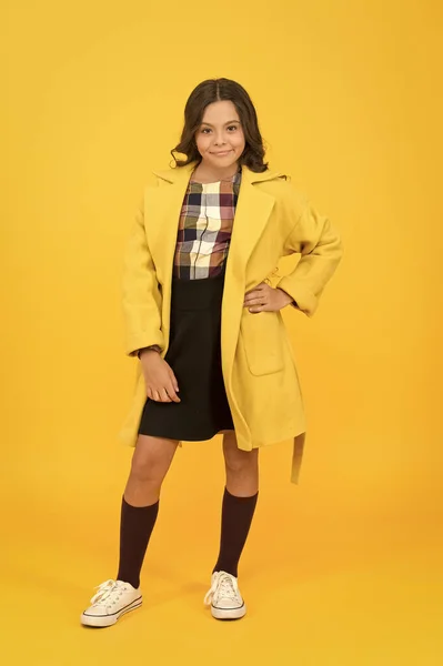 Udržujte ji vřelou a stylovou. Stylová dívka ve formálním kabátě chodí do školy. Malé dítě se stylovým podzimním vzhledem na žlutém pozadí. Stylový a pohodlný — Stock fotografie