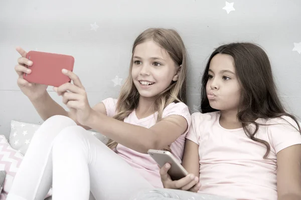 Dzieci robiące sobie selfie w sypialni. Koncepcja piżamy. Dziewczęce, szczęśliwe dzieciństwo. Dziewczyny długie włosy ze smartfonami wykorzystują nowoczesną technologię. Zróbmy sobie selfie. Wyślij zdjęcie znajomym social network — Zdjęcie stockowe