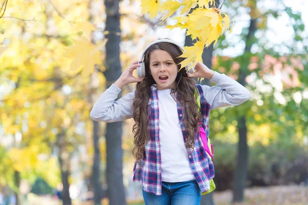 Menina irritada sofre de alta música desagradável som cacofonia no outono parque ao ar livre, fones de ouvido — Fotografia de Stock