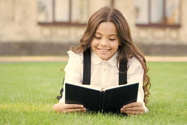Lectura extracurricular. Lindo niño pequeño leyendo libro al aire libre. Adorable niña aprender a leer. Colegiala uniforme escolar acostado en el césped con libro favorito. Estudiando el concepto. Educación básica — Foto de Stock