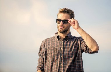 Net olarak gör. Yakışıklı adam güneş gözlüğü takıyor. Moda güneş gözlüklü hippi. Modaya uygun güneş gözlükleri. Ultraviyole koruma kavramı. Erkek gözlüklü model açık havada mavi gökyüzü arka planı. Mükemmel görüş