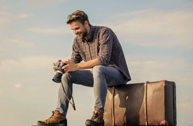 Görülecek dünya. Kameralı gazeteci. İş gezisi. Maço turist tur çantasına oturur. Gezgin, uçuşu bekle. Çekil şuradan. Seksi erkek gökyüzü arka planı. Erkek modası. Çok moda görünüyor.