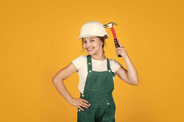 安全を確保しろ。ワークショップで修理してる女の子。ヘルメットの明るい子供はハンマーを保持します。大工と木工の概念です。ハンマーを使った10代の子供。道具を修理しています。修理人 — ストック写真