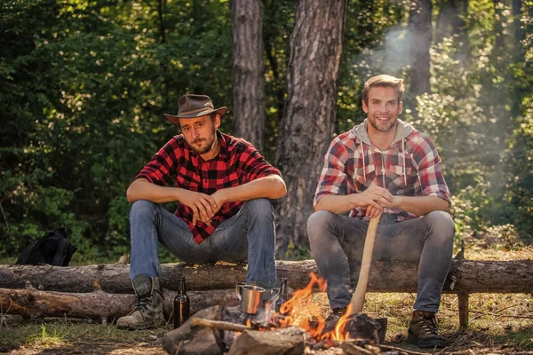 Scopri la vita. Concetto avventura. Escursione e persone. Due uomini si rilassano al fuoco. trekking e campeggio. amicizia maschile. L'uomo beve birra al falò. ranger alle attività all'aperto. trascorri un weekend di picnic nella natura — Foto Stock