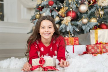 Noel ağacında suni kar üzerinde duran hediye kutusuyla mutlu küçük çocuk gülümsemesi, yeni yıl.