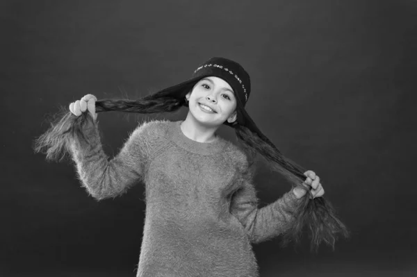 Το κυματιστό χτένισμα κερδίζει αυτή τη σεζόν. Ευτυχισμένο κορίτσι κρατήσει μελαχρινή μαλλιά κόκκινο φόντο. Το μικρό παιδί φοράει καπέλο σε μακρύ χτένισμα. Ωραίο χειμωνιάτικο χτένισμα. Δοκιμάστε νέα εμφάνιση και χτένισμα — Φωτογραφία Αρχείου