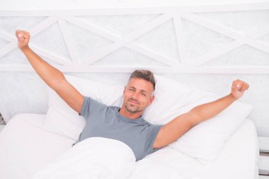 Genç adamın yatakta esnediğini gösteriyor. Adam yatakta geriniyor. Tasasız adam yeni günün tadını çıkarıyor. Uyan! Uyan! Pazar sabahının tadını çıkarıyorum. Tembel adam yatakta uyandığı için mutlu. Sabah yükselen eller