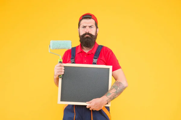 Érett szakállas fickó festő munkás kazán ruha egyenruha segítségével festék görgő eszköz festészet fal és tartsa táblán másolni tér reklám, reklám — Stock Fotó