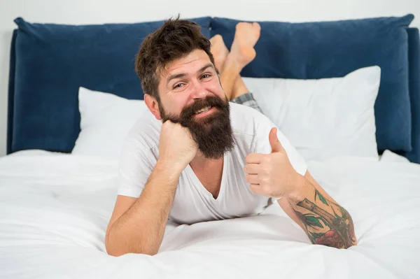 Mutlu sakallı adam evde yatakta rahatlar, güzel yatak odası konsepti. — Stok fotoğraf