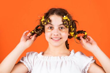 Şuna bak. Saç bigudileriyle poz ver. Kuaförde oynayan, saç bigudili mutlu kız. Çocuklar için saç stili yapmak için kolay ipuçları. Kuaför aletleri ve saç aksesuarları. Yüzü yamalı çocuk