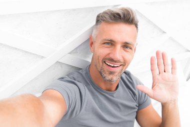 Merhabalar. Adam fotoğraf çeken akıllı telefondan el sallıyor. Çevrimiçi video yayınlanıyor. Gezici internet. Blog için çekim. Olgun bir blogcu. İnternet günlüğü içeriği. Kişisel blog konsepti. Günaydın.