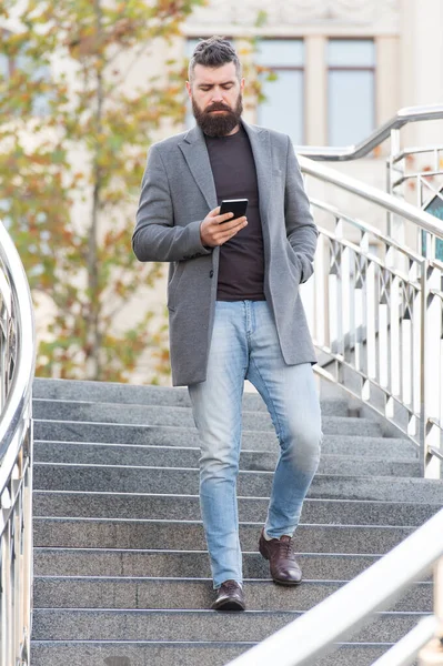 Общение является ключом к успеху в карьере. Бородатый мужчина читает смс на смартфоне, гуляя по городу. Коммуникации. 3G. 4G. Мобильные технологии. Современный стиль — стоковое фото