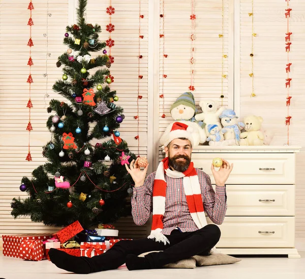 Man with beard in hat and scarf holds Christmas balls. — Stock Photo, Image