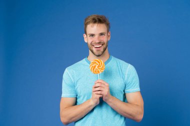 Çocukluk tadı. Tüylü adam lolipopu seviyor. Yemek konseptini aldatmak. Şeker sağlığa zararlıdır. Adamın elinde lolipop şeker menekşesi var. Yakışıklı maço adam kocaman renkli lolipop yiyor.