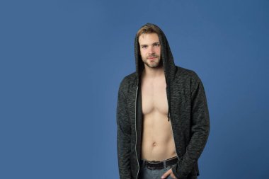 Sakallı adam menekşe arka planda kapüşon takıyor. Sıradan tişörtlü, seksi vücutlu bir maço. Kapüşonlu manken. Aktif yaşam tarzı ve sağlık aktiviteleri. Moda tarzı ve trend konsepti, alanı kopyala