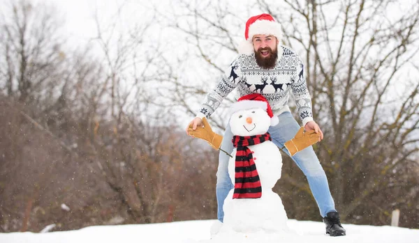 Warm clothes. happy hipster ready to celebrate. bearded man build snowman. man santa hat play with snow. winter season activity. its christmas. winter holiday outdoor. warm sweater in cold weather — Stock Photo, Image