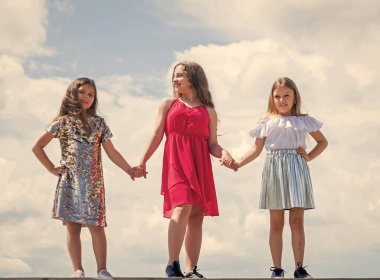 Sevgi ve destek. Kardeşlik ve arkadaşlık kavramı. Aile bağı kurma zamanı. Sonsuza kadar en iyi arkadaş. Gökyüzü arka planında üç kız kardeş. Mutlu çocukluk kavramı. Yaz tatili. Küçük kızlar el ele tutuşur
