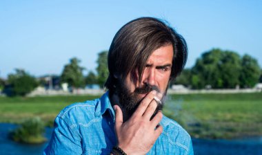 Bıyıklı vahşi sakallı hippi şık bir saç kesimi ve açık havada sigara içen sıradan bir gömlek giyiyor, rahatlıyor.