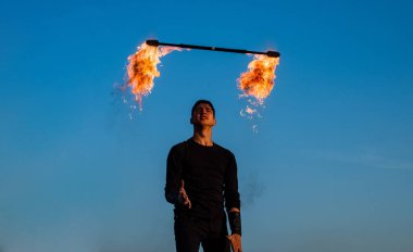 Açık havada mavi gökyüzünde yanan bastonla manipüle edilen erkek ateş sanatçısı.