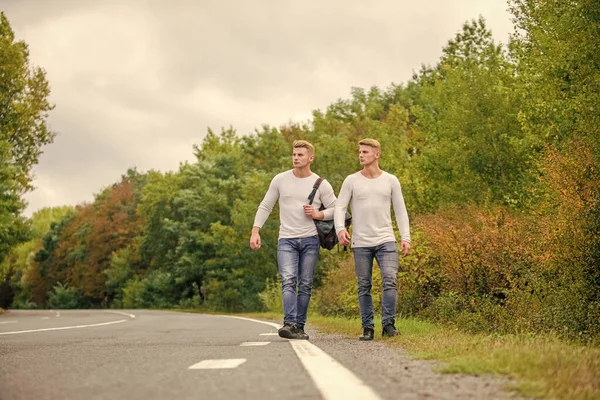 Guys hitchhiking on road. Tourist traveler travel auto stop. Transporting issues. Men backpack walking road. Twins walk along road. Brothers friends nature background. Long way. Adventure concept — Stock Photo, Image