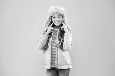 İçten bir gülümseme. Soğuk hava için sıcak şapka. Sahte kürk trendi. Uzun kıvırcık saçlı kız, pembe kulaklıklı kürk şapka takıyor. Yumuşak tüylü aksesuar. Çocuk uzun saçlı yumuşak kürk şapkalı Yumuşaklığın tadını çıkar