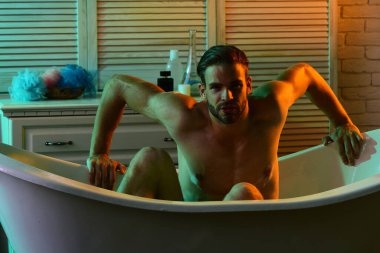 Güçlü kolları olan, küvette çıplak oturan maço.