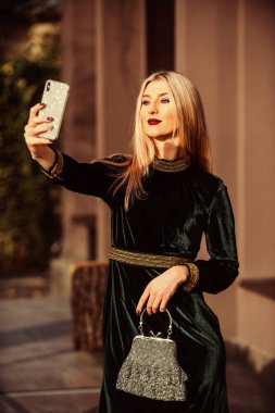 Yeni tarzını seviyor. Moda blogu. Zarif yeşil kadife elbise. Cazip kadife tekstil. Seksi iş kadını telefonda selfie çekiyor. Modern hayat. Kızlar için değerli taş bir çanta. glam debriyaj aksesuarı