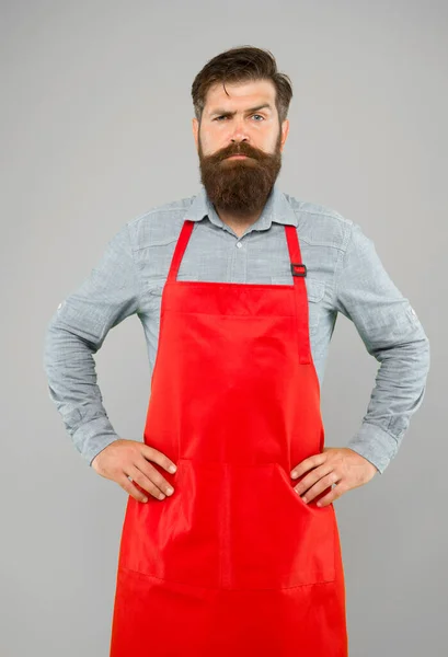 Chef barbudo ou garçom usando avental vermelho. empregado de mesa brutal ou barista. Um barbeiro de avental com barba comprida. Bonito mestre confiante. Empreendedor em seu olhar moderno — Fotografia de Stock