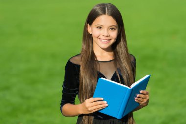 Mutlu küçük çocuk kütüphane kitabı okuyor. Yeşil çimen, açık hava, okul.