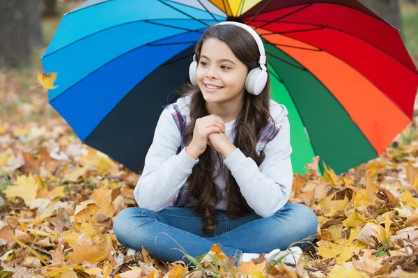 Czuję się chroniony. Jesienny dzieciak pod kolorowym parasolem. Poczuj inspirację. Szczęśliwego dzieciństwa. Z powrotem do szkoły. Dziewczyna w słuchawkach w parku. cieszyć się jesienią w lesie. Słuchaj muzyki. edukacja online — Zdjęcie stockowe