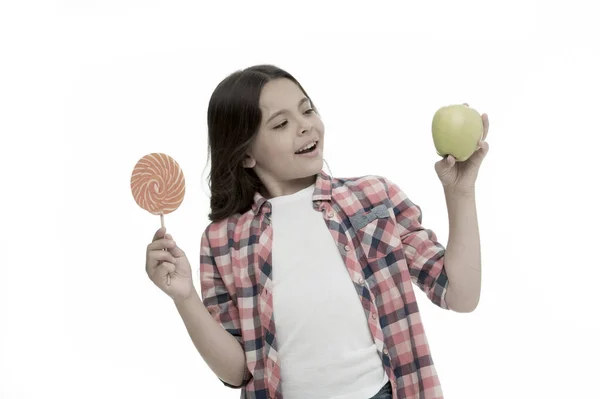 Zdrowa alternatywa. Słodki smak może nas uszczęśliwić. Dziewczyna trzyma słodki lizak i jabłko. Szkolna alternatywa. Dziewczyna wybrać cukierki lub owoce odizolowane biały. Ten sam słodki smak jabłka i słodyczy — Zdjęcie stockowe