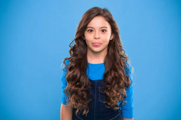 Volume de cabelo extremo. Miúdo menina longo cabelo brilhante saudável. Kid rosto bonito feliz com penteado encaracolado adorável ficar sobre fundo azul. Ensinar hábitos saudáveis de cuidado do cabelo. Menina crescer cabelos longos — Fotografia de Stock