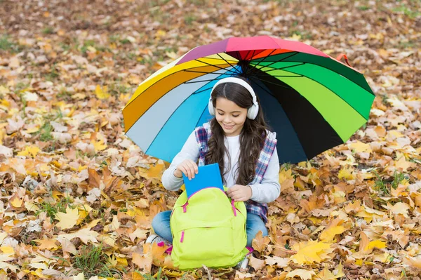 going to read the book. happy childhood. back to school. girl in headset with backpack relax in park. enjoy fall in forest. listen to music. online courses education. autumn kid under umbrella