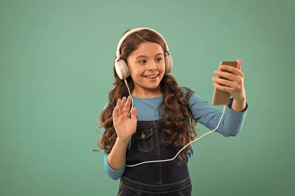 hello. kid long hair make selfie in headset. small child make play list on smartphone. small girl use mp3 player. study in modern life. schoolgirl use digital device. casual fashion for kids
