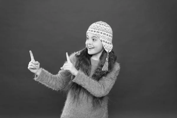 Señalando así. Traje de invierno. Lindo modelo disfrutar del estilo de invierno. Niño pequeño pelo largo usar sombrero fondo rojo. Concepto de invierno. Un niño pequeño usa un sombrero de punto. Niña accesorio de moda de invierno — Foto de Stock