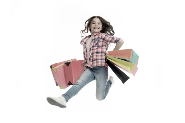 Szczęśliwa dziewczyna skakać z torby na zakupy izolowane na białym. Mały, zakupoholiczny uśmiech z papierowymi torbami. Dziecięca moda. Zakupy i sprzedaż. Urlop urodzinowy. Czarny piątek. Zabawa w ruchu — Zdjęcie stockowe