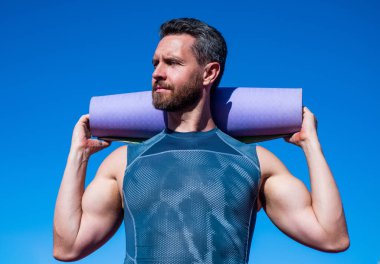 Gökyüzü arka planında yoga minderi olan pilates eğitmeni, spor