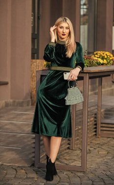 Kız el çantası taşıyor. Göz alıcı debriyaj aksesuarı. Moda blogu. Yeşil kadife elbiseli zarif bir kadın. Kadife moda trendi. İpek kadife. Cazibeli kadife tekstil. Açık havada seksi bir kadın. modern yaşam